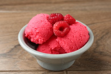 Photo of Delicious raspberry sorbet with fresh berries in bowl on wooden table, closeup