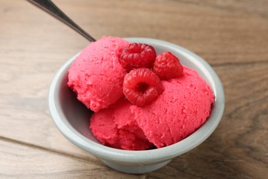 Photo of Delicious raspberry sorbet with fresh berries in bowl on wooden table, closeup
