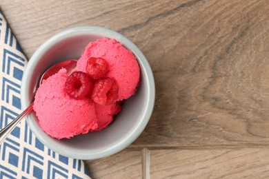 Photo of Delicious raspberry sorbet with fresh berries and spoon in bowl on wooden table, top view. Space for text