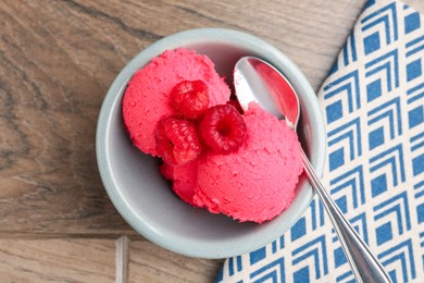 Photo of Delicious raspberry sorbet with fresh berries and spoon in bowl on wooden table, top view