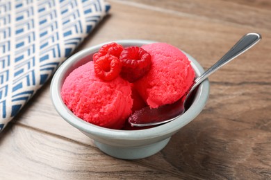 Photo of Delicious raspberry sorbet with fresh berries and spoon in bowl on wooden table, closeup