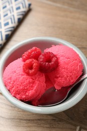 Photo of Delicious raspberry sorbet with fresh berries and spoon in bowl on wooden table, closeup