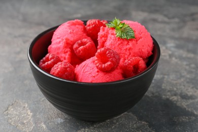 Photo of Delicious raspberry sorbet with fresh berries and mint in bowl on grey textured table, closeup
