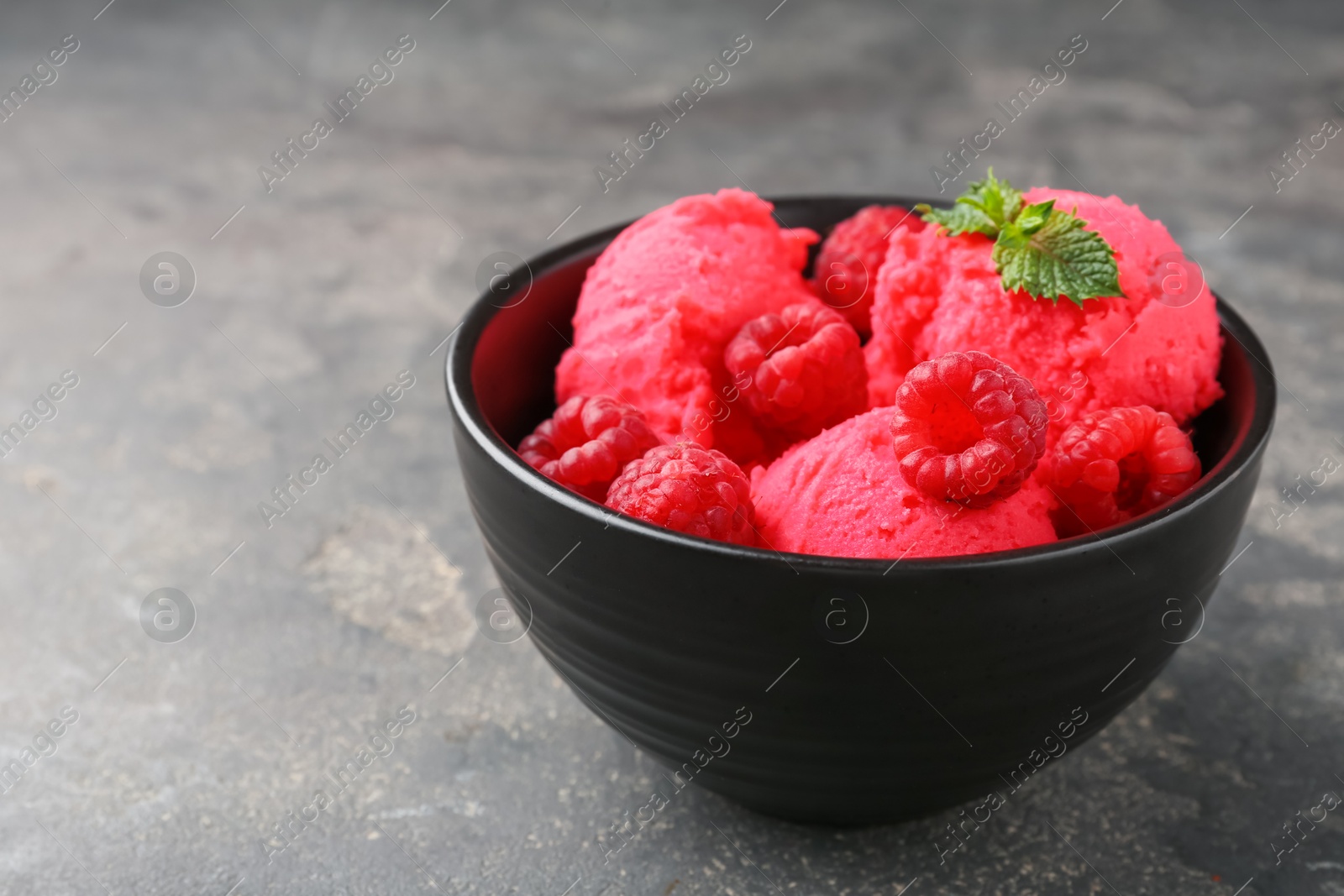 Photo of Delicious raspberry sorbet with fresh berries and mint in bowl on grey textured table, closeup. Space for text