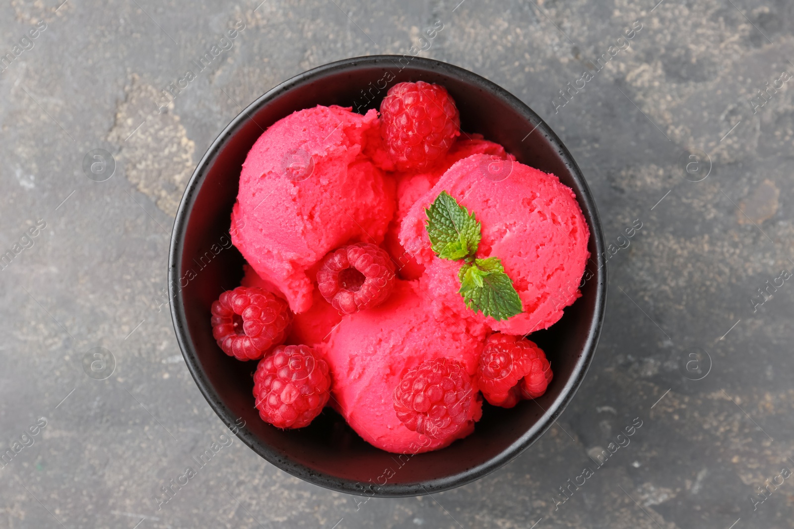 Photo of Delicious raspberry sorbet with fresh berries and mint in bowl on grey textured table, top view