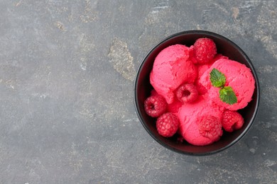 Photo of Delicious raspberry sorbet with fresh berries and mint in bowl on grey textured table, top view. Space for text