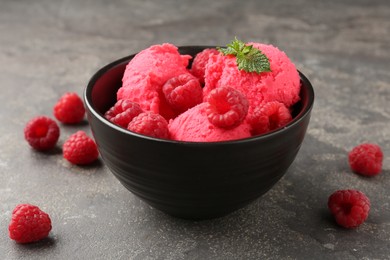 Photo of Delicious raspberry sorbet with fresh berries and mint in bowl on grey textured table, closeup