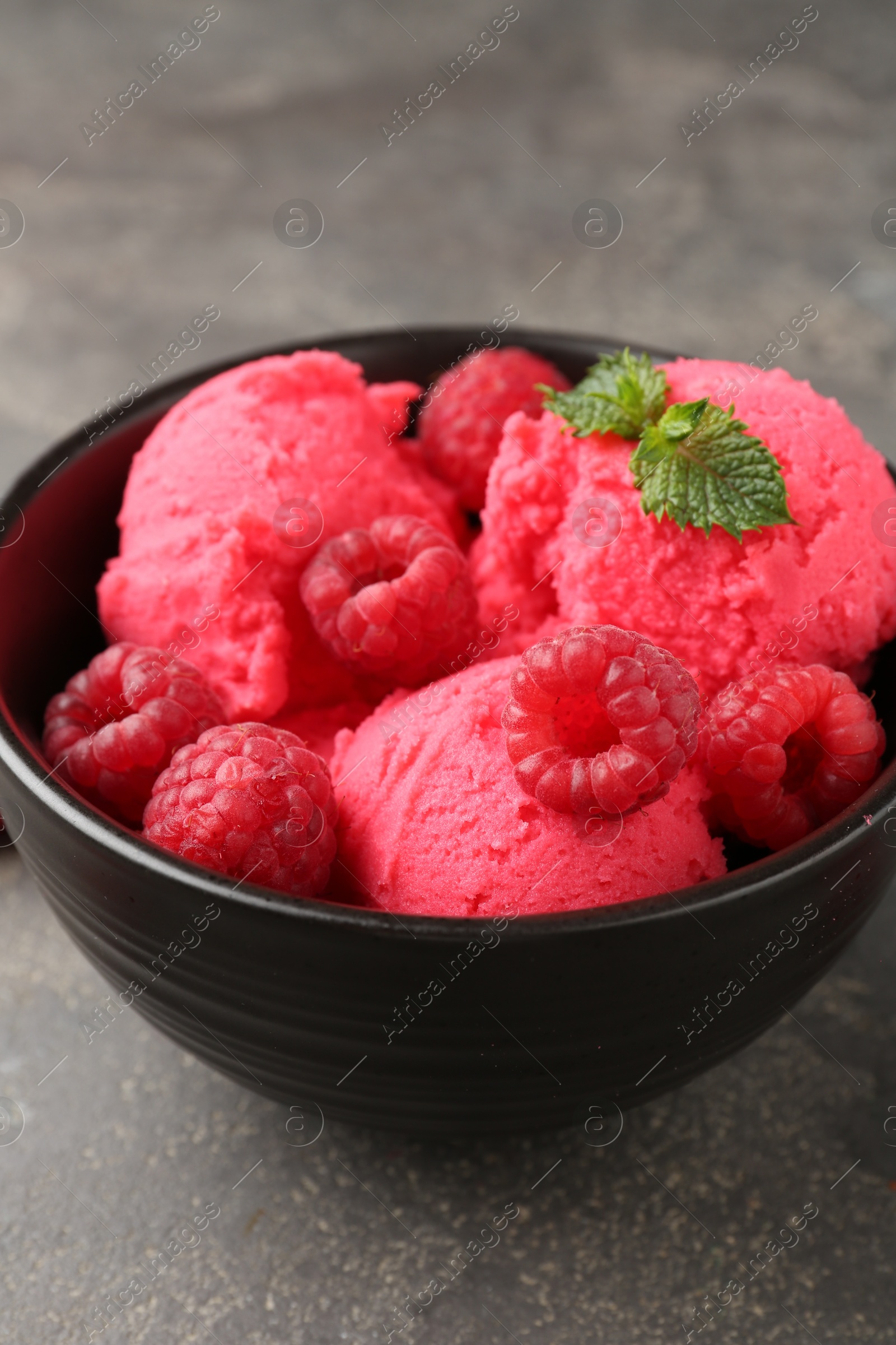 Photo of Delicious raspberry sorbet with fresh berries and mint in bowl on grey textured table, closeup