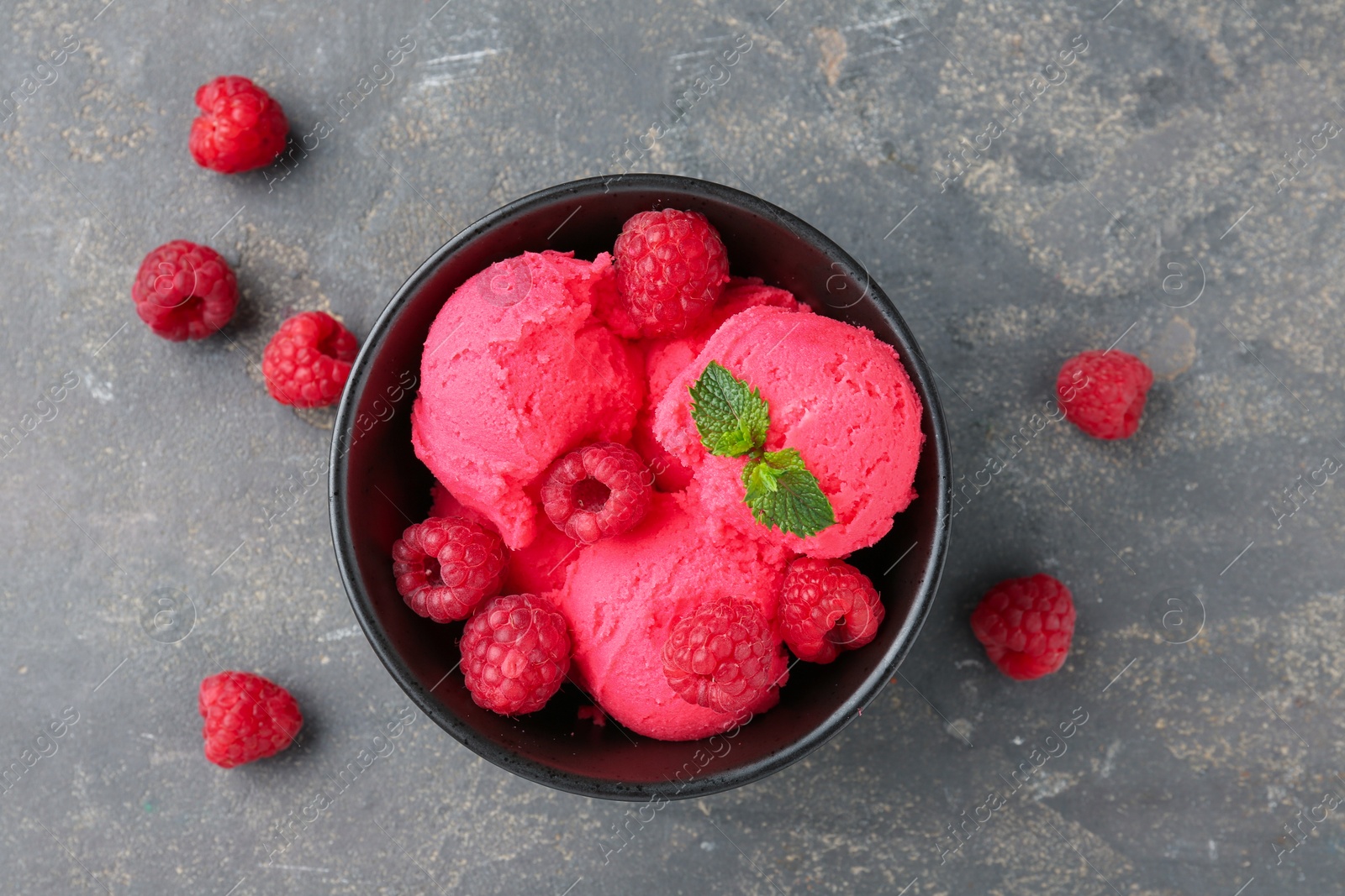 Photo of Delicious raspberry sorbet with fresh berries and mint in bowl on grey textured table, flat lay
