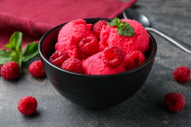 Photo of Delicious raspberry sorbet with fresh berries and mint in bowl on grey textured table, closeup