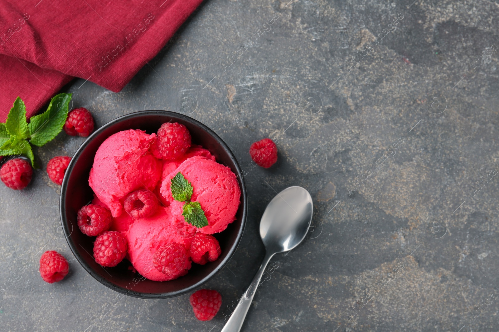Photo of Delicious raspberry sorbet with fresh berries and mint in bowl served on grey textured table, flat lay. Space for text