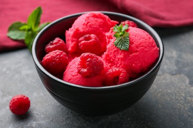 Photo of Delicious raspberry sorbet with fresh berries and mint in bowl on grey textured table, closeup