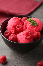 Photo of Delicious raspberry sorbet with fresh berries and mint in bowl on grey textured table, closeup