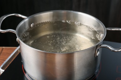 Photo of Metal pot with boiling water on stove in kitchen, closeup
