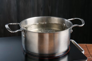 Photo of Metal pot with boiling water on stove in kitchen, closeup