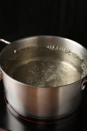 Photo of Metal pot with boiling water on stove in kitchen, closeup