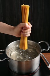 Photo of Woman putting tagliatelle pasta into pot on electric stove in kitchen, closeup