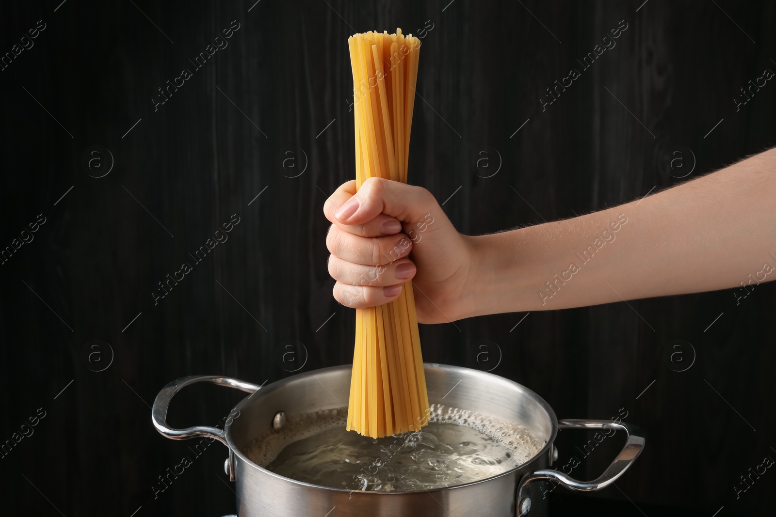 Woman putting tagliatelle pasta into pot on electric stove in kitchen, closeup Photo of Woman putting tagliatelle pasta into pot on electric stove in kitchen, closeup