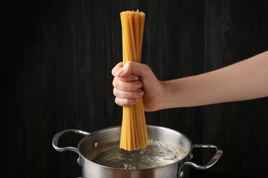 Photo of Woman putting tagliatelle pasta into pot on electric stove in kitchen, closeup