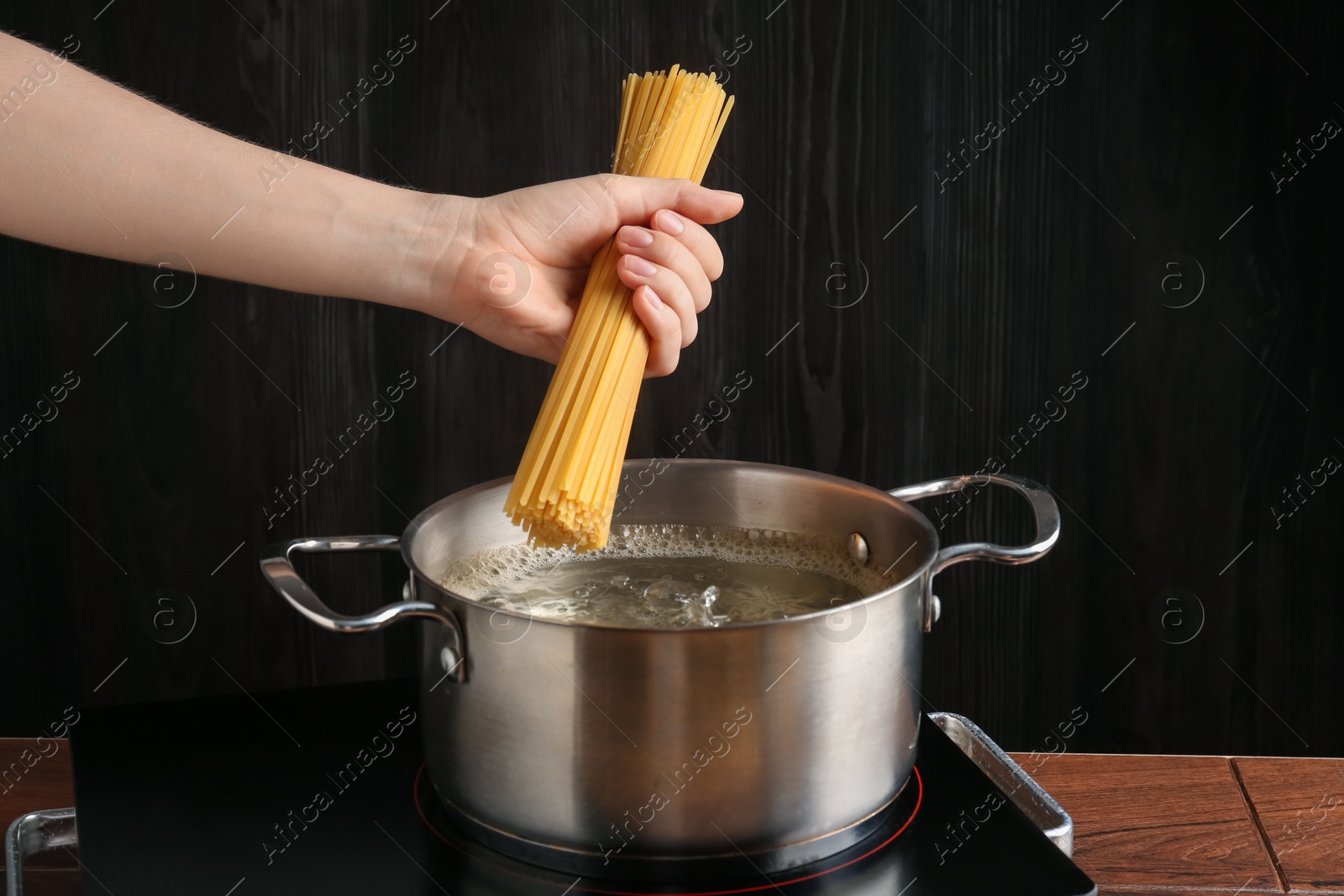 Woman putting tagliatelle pasta into pot on electric stove in kitchen, closeup Photo of Woman putting tagliatelle pasta into pot on electric stove in kitchen, closeup