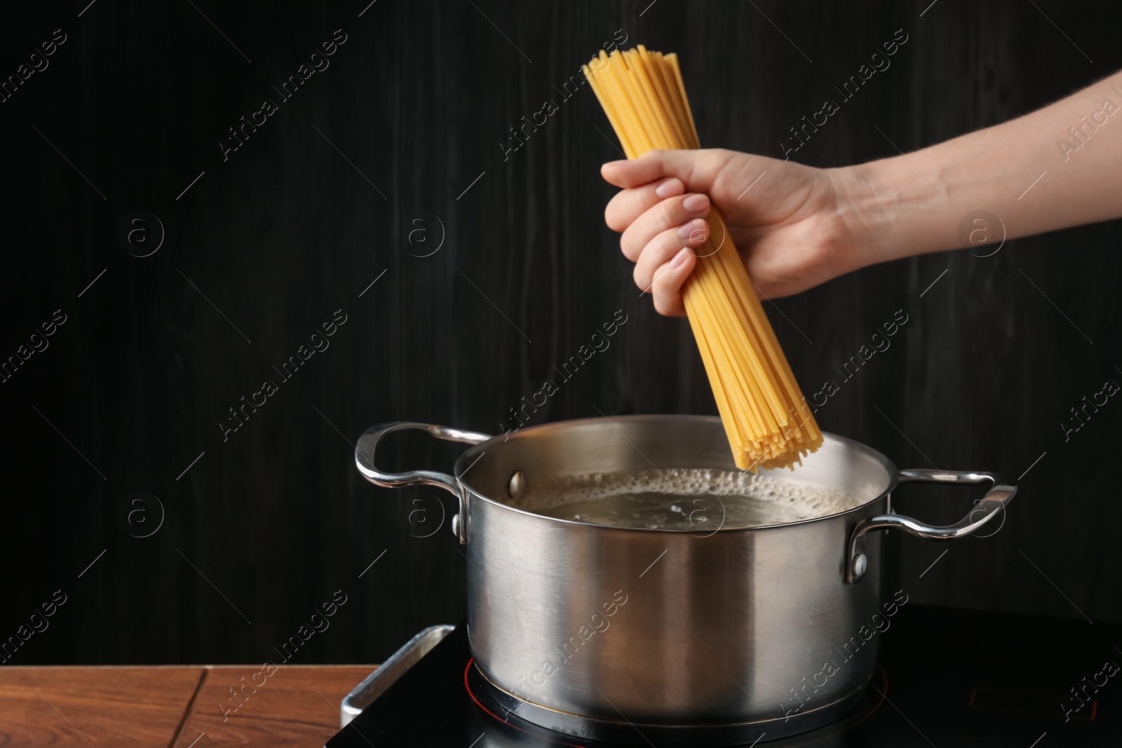 Woman putting tagliatelle pasta into pot on electric stove in kitchen, closeup Photo of Woman putting tagliatelle pasta into pot on electric stove in kitchen, closeup