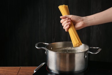 Photo of Woman putting tagliatelle pasta into pot on electric stove in kitchen, closeup