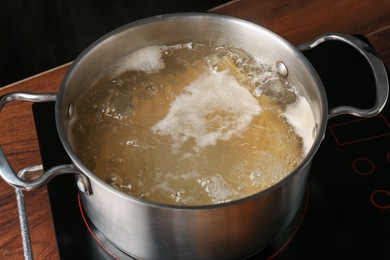 Photo of Fresh tagliatelle pasta boiling in pot with water on electric stove, closeup