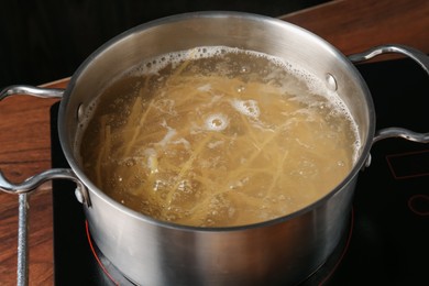 Photo of Fresh tagliatelle pasta boiling in pot with water on electric stove, closeup