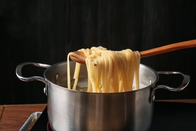 Photo of Taking boiled tagliatelle pasta with spoon from pot on electric stove, closeup