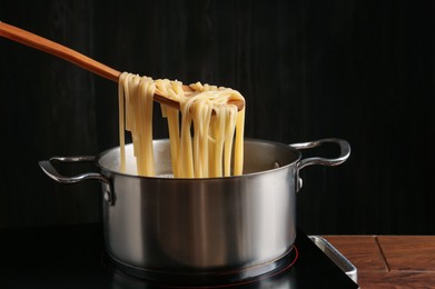 Photo of Taking boiled tagliatelle pasta with spoon from pot on electric stove, closeup