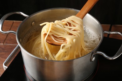 Photo of Taking boiled tagliatelle pasta with spoon from pot on electric stove, closeup