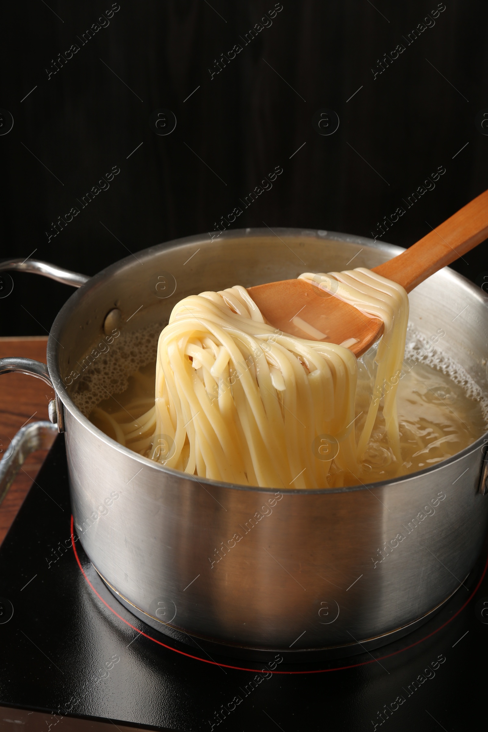 Taking boiled tagliatelle pasta with spoon from pot on electric stove, closeup Photo of Taking boiled tagliatelle pasta with spoon from pot on electric stove, closeup