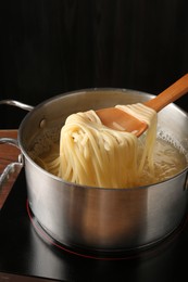 Photo of Taking boiled tagliatelle pasta with spoon from pot on electric stove, closeup