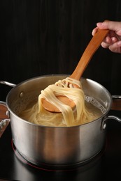 Photo of Woman taking boiled tagliatelle pasta with spoon from pot on electric stove, closeup