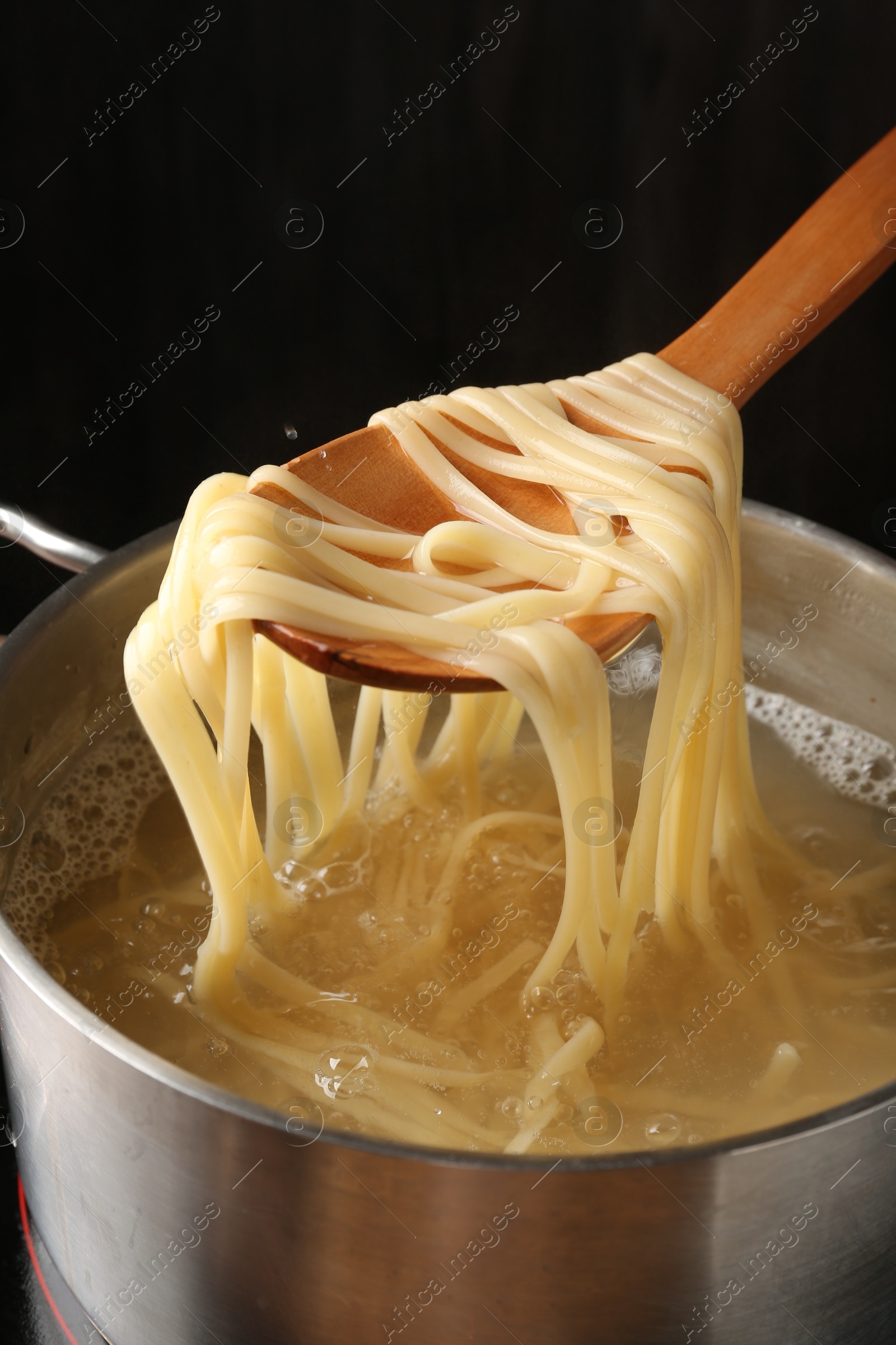 Taking boiled tagliatelle pasta with spoon from pot on electric stove, closeup Photo of Taking boiled tagliatelle pasta with spoon from pot on electric stove, closeup