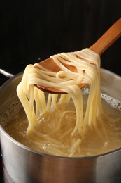 Photo of Taking boiled tagliatelle pasta with spoon from pot on electric stove, closeup