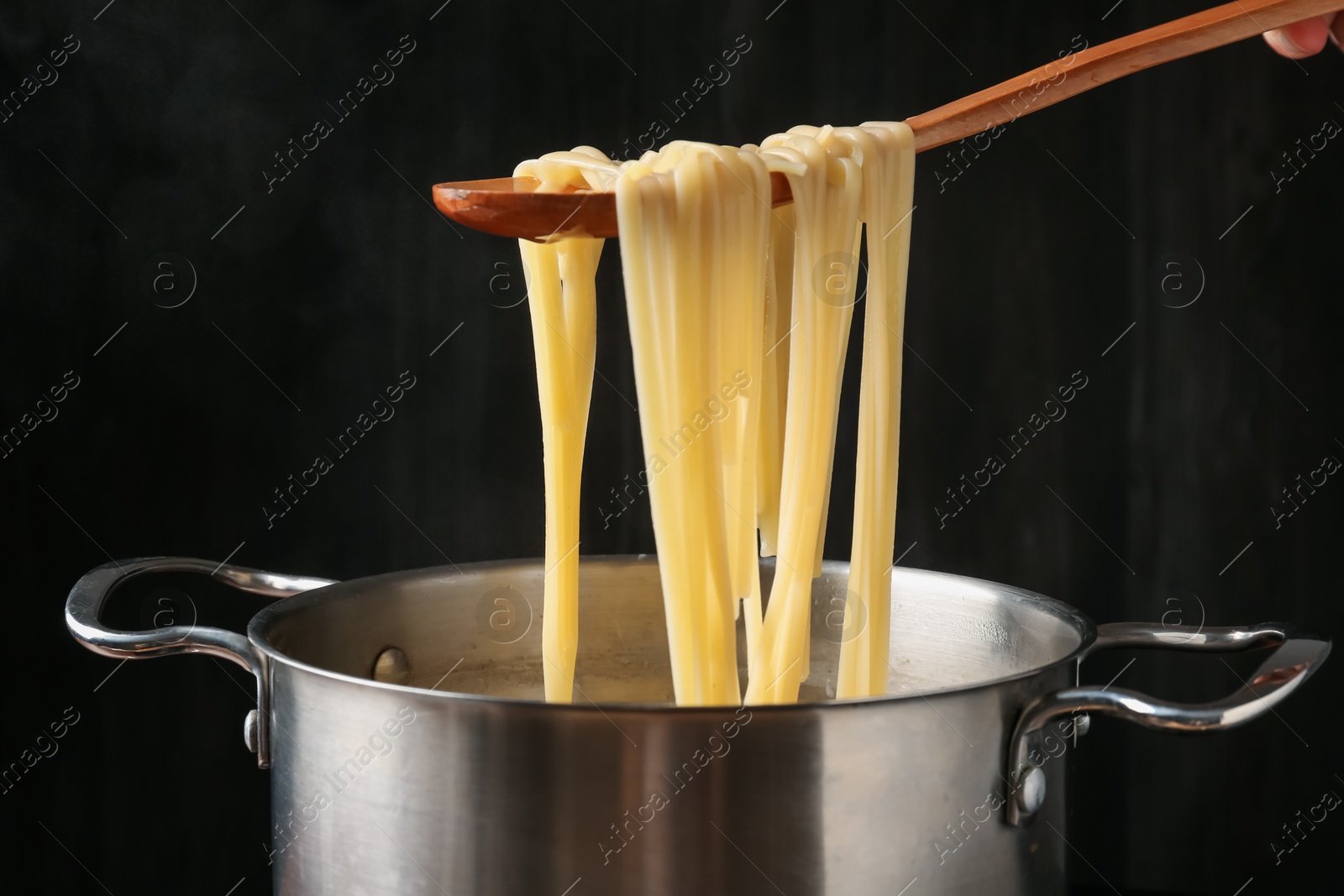 Taking boiled tagliatelle pasta with spoon from pot on electric stove, closeup Photo of Taking boiled tagliatelle pasta with spoon from pot on electric stove, closeup