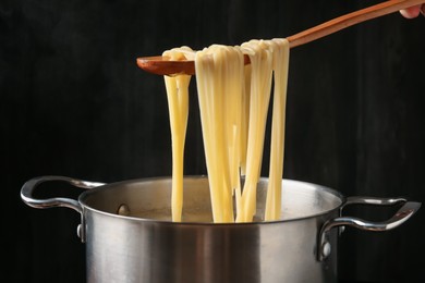 Photo of Taking boiled tagliatelle pasta with spoon from pot on electric stove, closeup