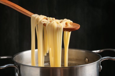 Photo of Taking boiled tagliatelle pasta with spoon from pot on electric stove, closeup