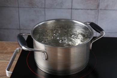 Photo of Metal pot with boiling water on stove in kitchen, closeup
