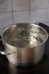 Photo of Metal pot with boiling water on stove in kitchen, closeup