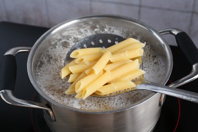 Photo of Taking cooked penne pasta from pot with boiling water on electric stove, closeup