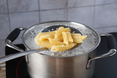 Photo of Taking cooked penne pasta from pot with boiling water on electric stove, closeup
