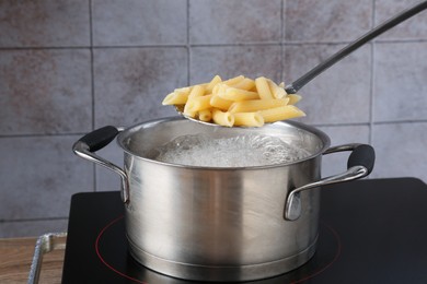 Photo of Taking cooked penne pasta from pot with boiling water on electric stove, closeup