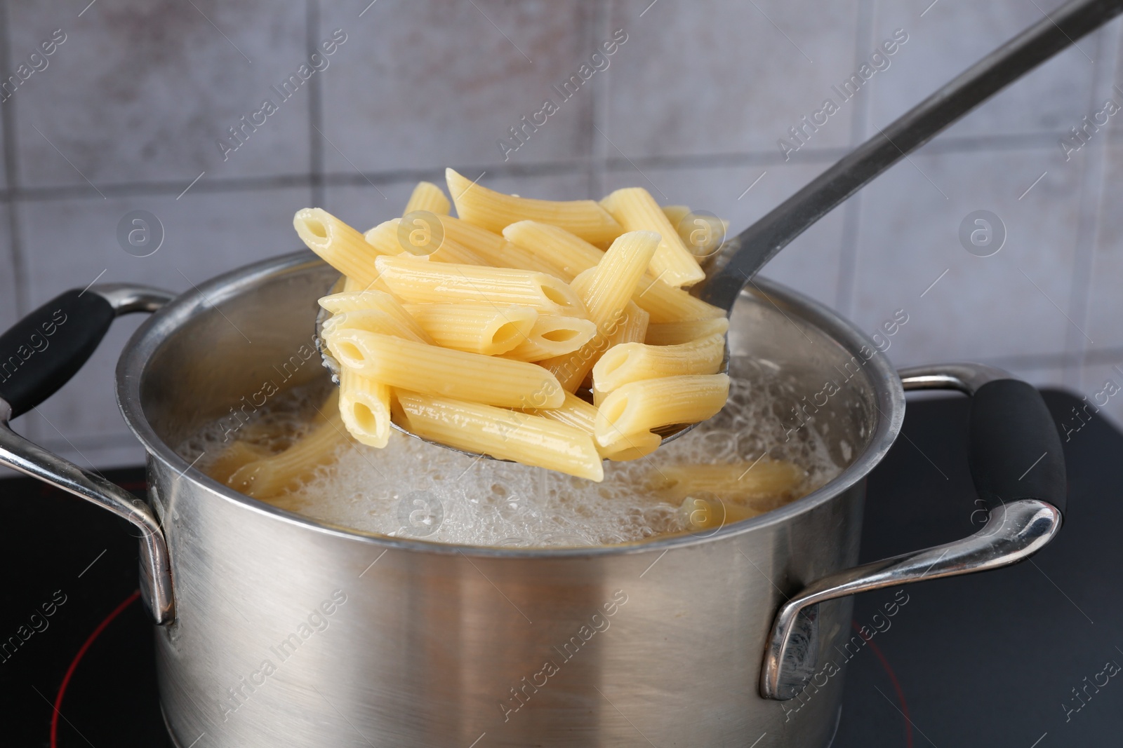 Taking cooked penne pasta from pot with boiling water on electric stove, closeup Photo of Taking cooked penne pasta from pot with boiling water on electric stove, closeup