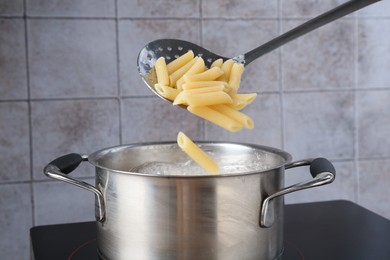 Photo of Putting cooked penne pasta into pot with boiling water on electric stove, closeup