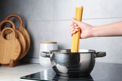 Photo of Woman putting tagliatelle pasta into pot on electric stove in kitchen, closeup