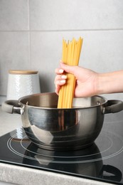 Photo of Woman putting tagliatelle pasta into pot on electric stove in kitchen, closeup