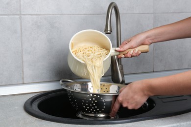 Photo of Woman draining boiled tagliatelle pasta into colander at sink in kitchen, closeup