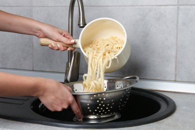 Photo of Woman draining boiled tagliatelle pasta into colander at sink in kitchen, closeup